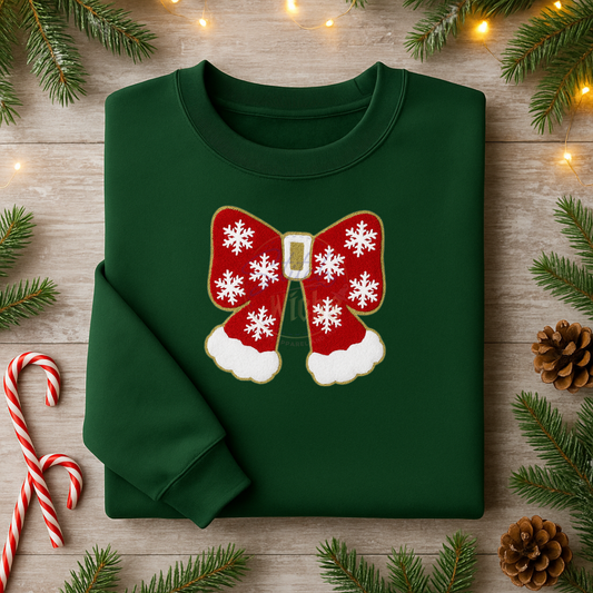 Green sweatshirt with a red bow design on a wooden surface with Christmas decorations.